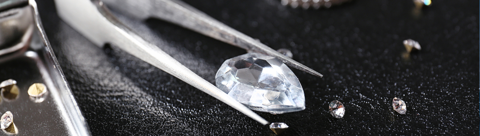close up of a large pear shapped diamond behind held by a metalic jeweler's tool